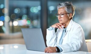 A female physician is participating in a virtual medical education session on her laptop