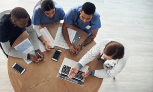 A diverse group of male and female healthcare providers are centered around a computer as part of a virtual publication planning project