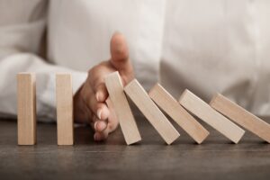 A hand is stopping a domino of jenga block to illustrate the concept of "barriers"